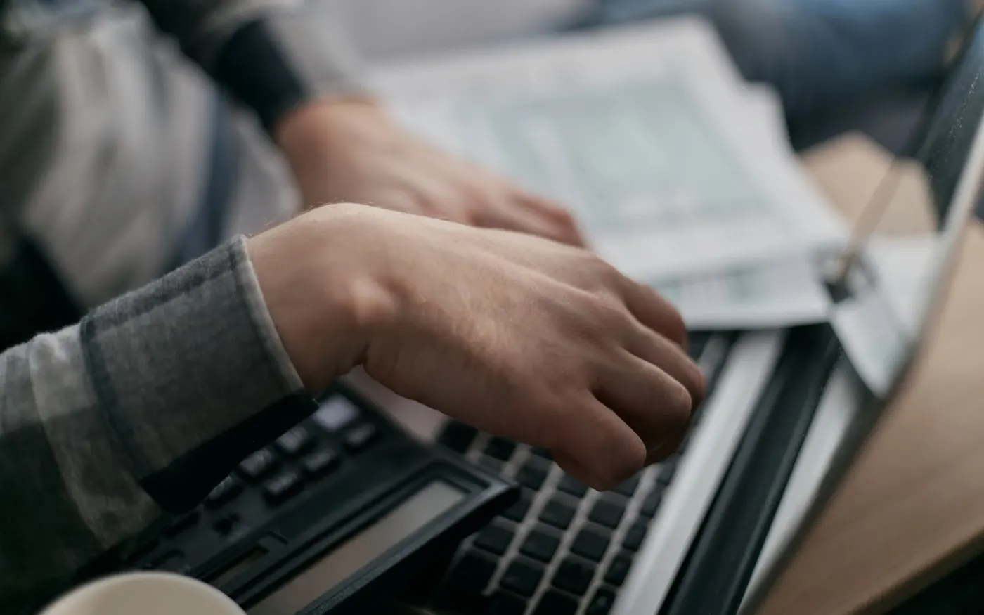 Manos escribiendo en el teclado de un portátil junto a la documentación de facturación