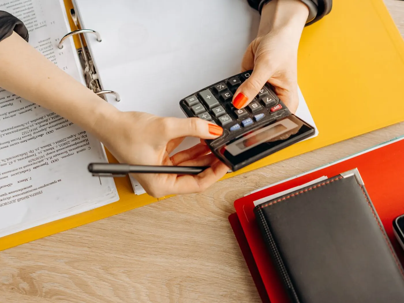 Manos usando una calculadora sobre el archivador con la documentación de un cliente